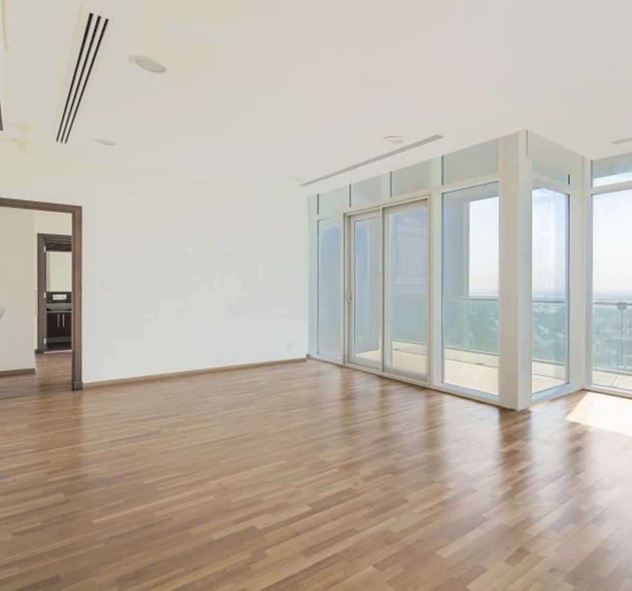 Empty main room with wood floor, white walls, and a corner of floor-to-ceiling glass windows and balcony doors.