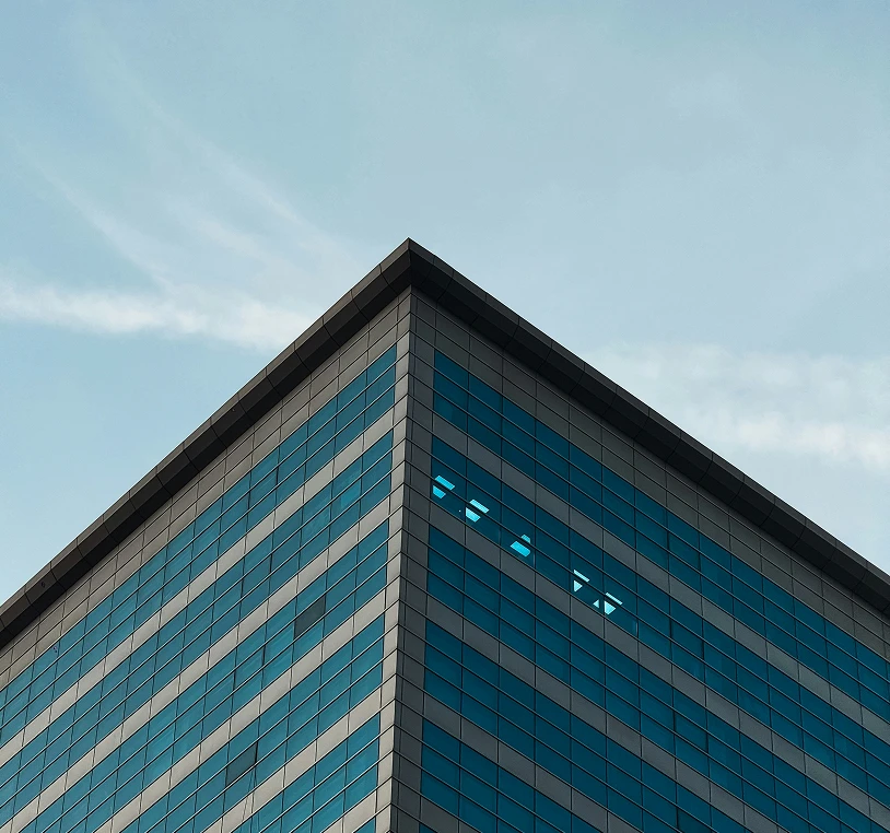 Low-angle view of the sharp corner of a modern office building with a blue glass facade.