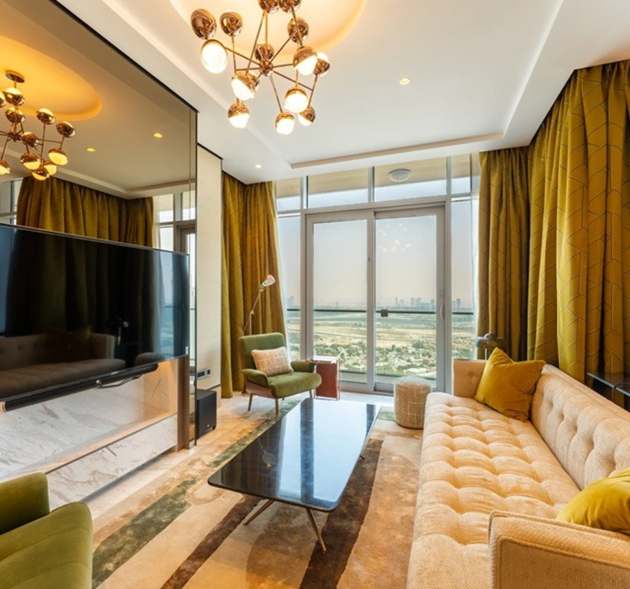 Opulent living room featuring a beige sofa, green accent chairs, a Sputnik chandelier, and full-height windows with a city view.