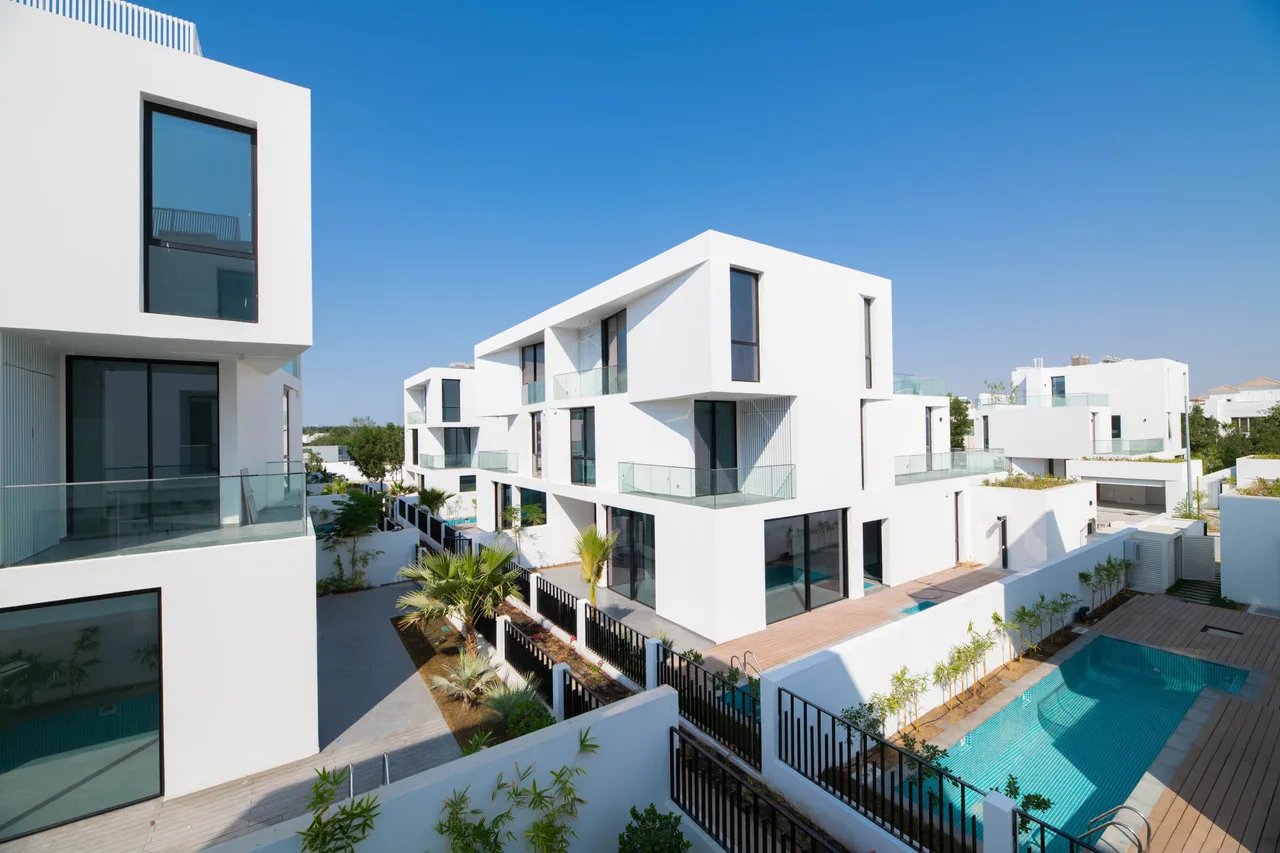 Wide exterior view of a modern residential complex featuring multiple white cubic villas with large windows and private pools.